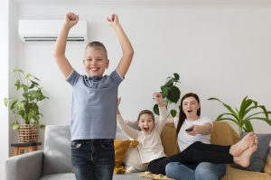 une femme et ses deux enfants sautant de joie dans une pièce avec un climatiseur
